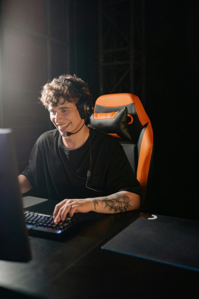 Smiling young man playing games on PC with headphones, enjoying a thrilling gaming session.